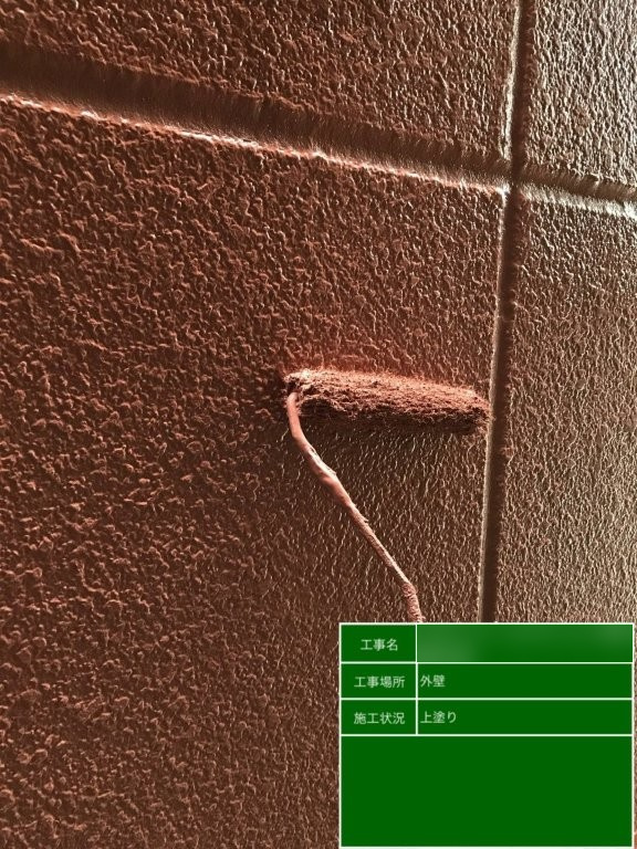 足立区南花畑 Fマンションの赤茶系外壁をローラーで上塗りしている様子